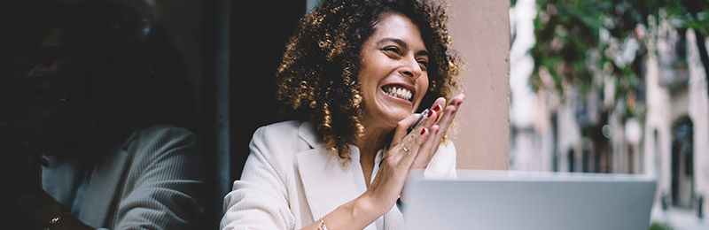 Female entrepreneur clapping her hands while sitting in front of her computer as she crafts compelling messages within her business plan.