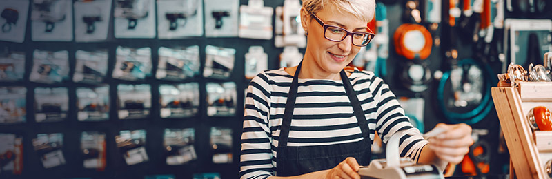 Female entrepreneur standing at the front of her shop reviewing receipts to start organizing categories for a sales forecast.