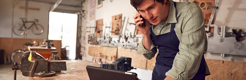 Male entrepreneur standing at the front desk of his shop checking on the shipping and fulfillment status of his current products.